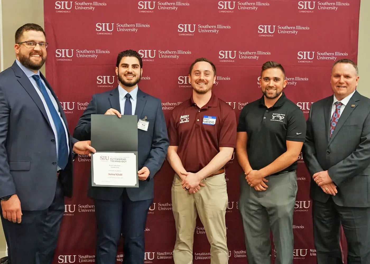 Group of people standing in front of a Southern Illinois University backdrop, with one person holding an award.